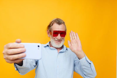 Senior man doing selfie against yellow background