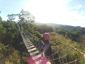 Woman walking on rope bridge over lush foliage