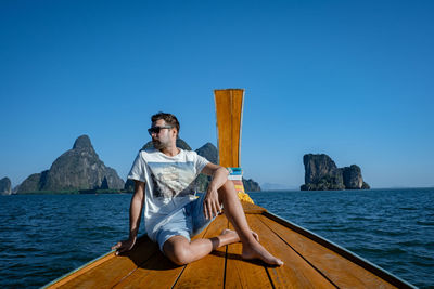 Man sitting on boat in sea against clear sky