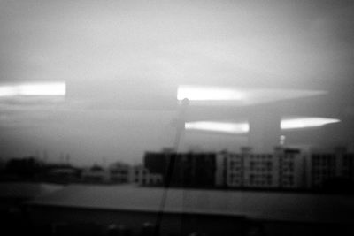 Defocused image of building against sky seen through glass window