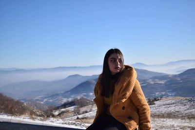 Young woman sitting on cliff against mountains during winter