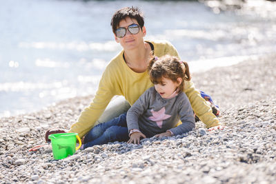 Full length of mother and daughter playing with pebbles at beach