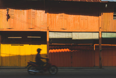 Lowlight photography light shadow - motion blur of man on a motorbike in front closed shop houses