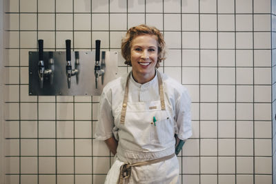 Portrait of smiling young woman standing against wall