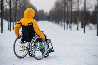 Rear view of man riding bicycle on snow covered field