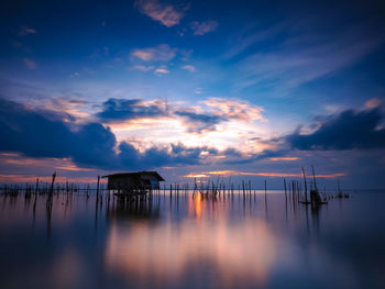 Silhouette wooden posts in sea against sky at sunset