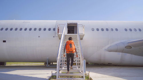 Rear view of man climbing on abandoned airplane against sky