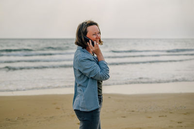 A young woman on the beach near the ocean in the spring at sunset talking on the phone with a smile