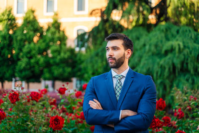 Portrait of young man standing against pink flowering plants