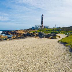 Lighthouse on beach by buildings against sky