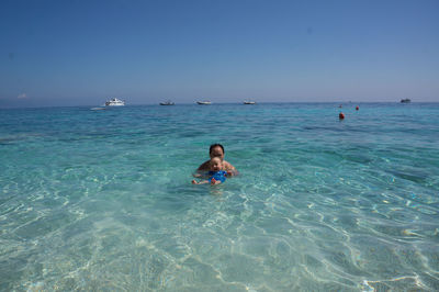 Father with son enjoying in sea against clear blue sky during sunny day