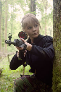 Young woman with sniper by tree at forest