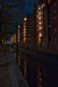 Illuminated street by buildings at night