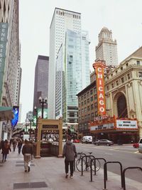 People on street amidst buildings in city against sky