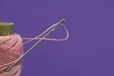 Close-up of sewing needle with thread spool against colored background