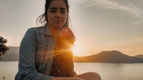 Portrait of smiling woman against lake during sunset