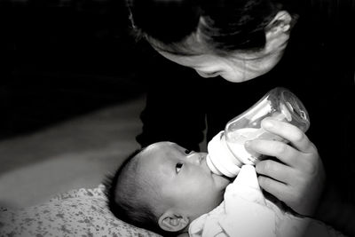 Mother feeding milk to cute daughter from bottle at home