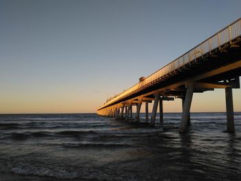 Pier over sea against clear sky at sunset