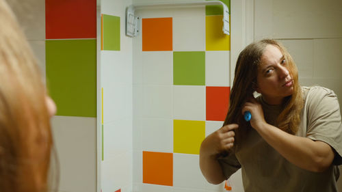 A girl standing in the bathroom against the mirror brushing her long, wet hair