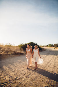 Friends walking on dirt road against sky