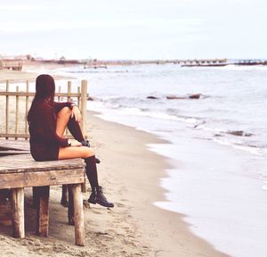 Side view full length of woman sitting on table at beach