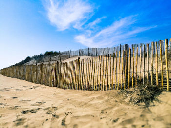 Fence on sand against sky