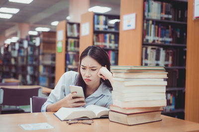 Young woman using phone while sitting with books on table