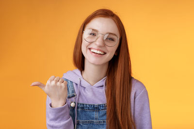 Woman in hooded shirt showing thumbs up against yellow background