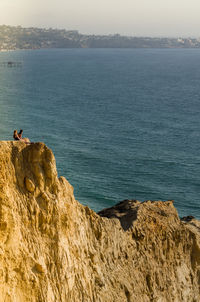 Man sitting on rock by sea against sky