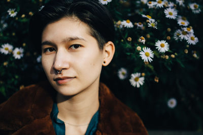 Portrait of woman in jacket standing against daisy flowering plants