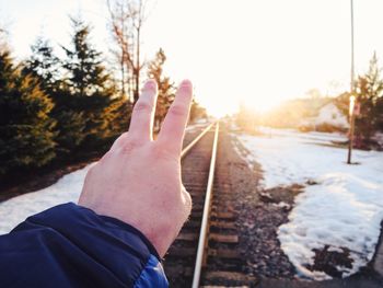 Cropped hand gesturing against railroad track