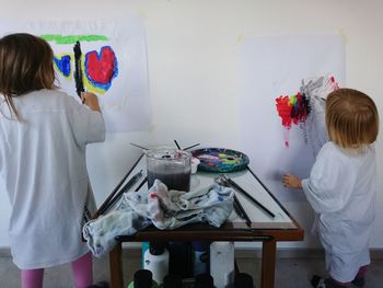 Rear view of siblings painting while standing against wall