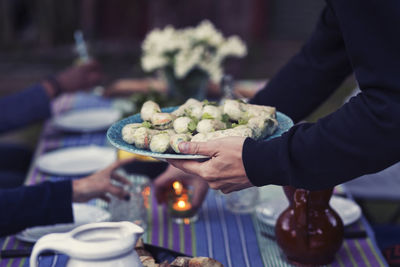 Cropped image of man holding plate with rice paper rolls at outdoor food table during party