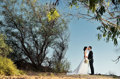 Full length of happy young woman with arms raised against trees