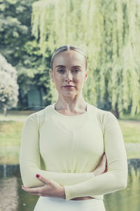 A young beautiful slender girl with long blonde hair does yoga in the summer in nature by the pond