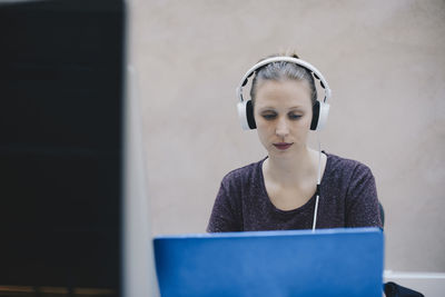 Female computer programmer wearing headphones while using laptop in office