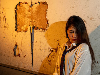 Young woman wearing shirt and tie standing against abandoned wall