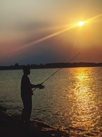 Silhouette man standing in sea against sky during sunset