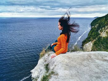 Woman standing on rock by sea against sky