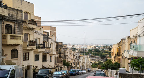 Cars on road by buildings in city against sky