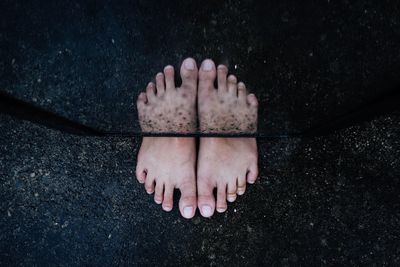 Low section of person standing by mirror reflection on footpath