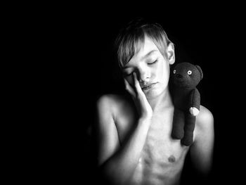 Shirtless boy with toy standing against black background