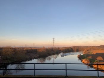 Electricity pylon by trees against sky during sunset