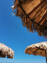 Low angle view of thatched roofs against clear blue sky