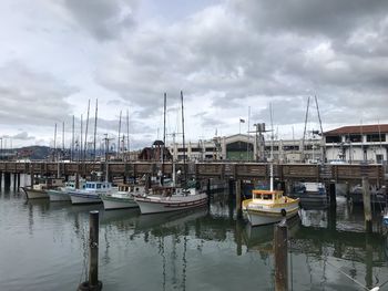 Boats moored in harbor against cloudy sky