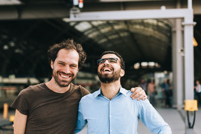 Happy friends laughing while standing at railroad station platform