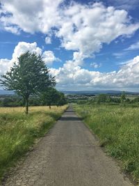 Road passing through field against cloudy sky