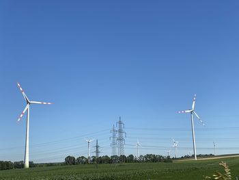 Wind turbines on field against clear blue sky