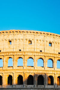 Low angle view of coliseum against clear blue sky on sunny day