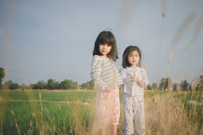 Portrait of cute sisters standing on grassy field against sky